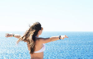海に向かって両手を広げる水着姿の女性