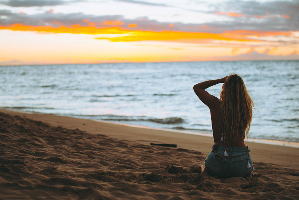 砂浜で夕焼けを見つめる女性